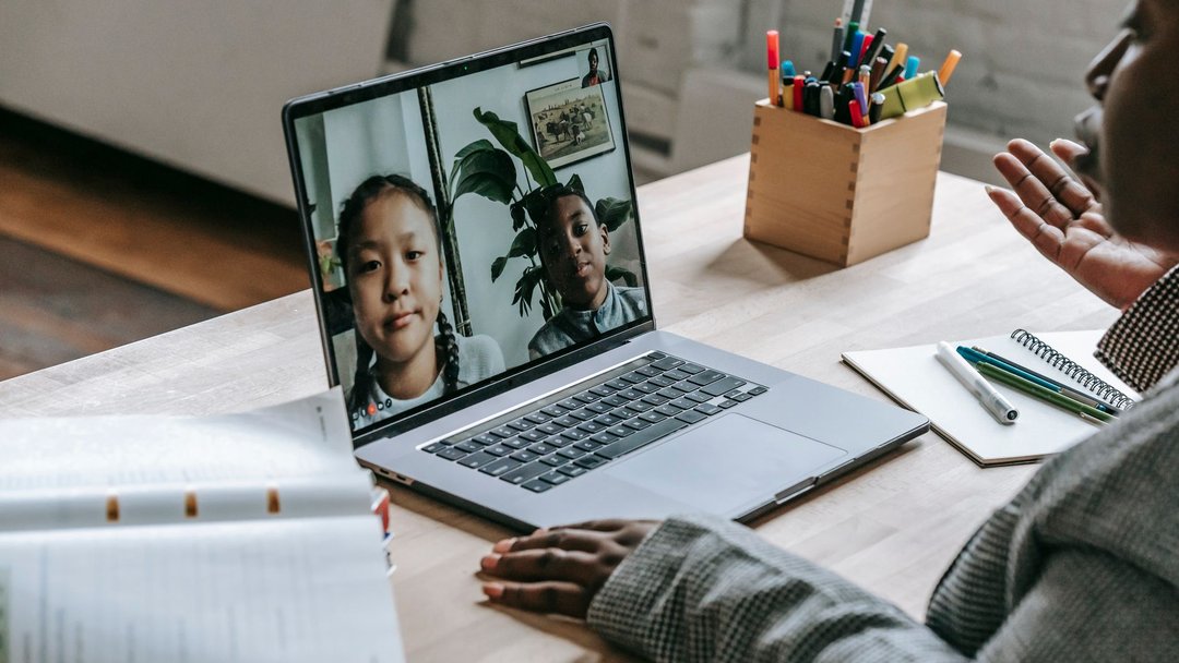 图 / Pexels · Katerina Holmes From above of crop confident African American female teacher sitting in classroom and teaching multiethnic pupils remotely on laptop during