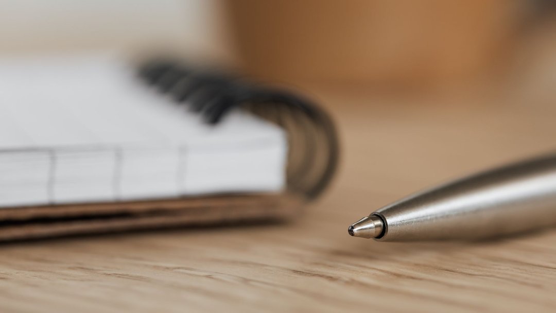 Side view closeup of opened ring bound notebook with blank pages near silver ball point pen placed on wooden table