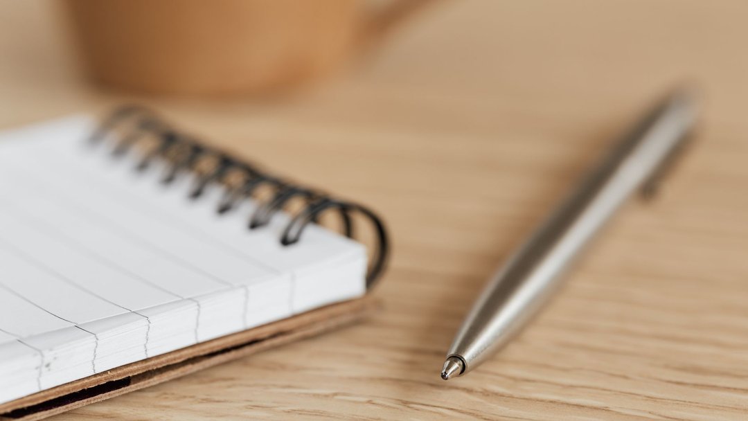 A detailed close-up photograph of a notepad and pen resting on a wooden desk.