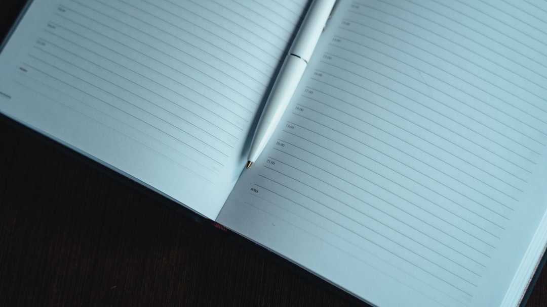 A neatly lined open notebook with a white pen on a dark wooden table, ready for notes.