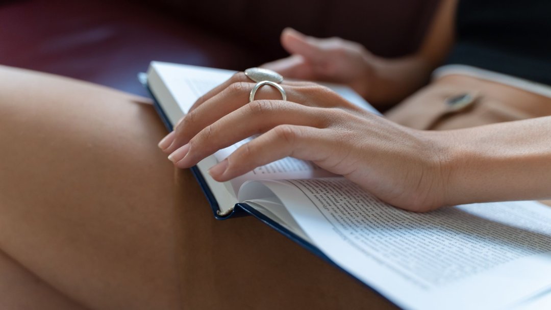 图 / Pexels · Yaroslav Shuraev A person reading a book indoors, capturing a close-up of hands turning pages.