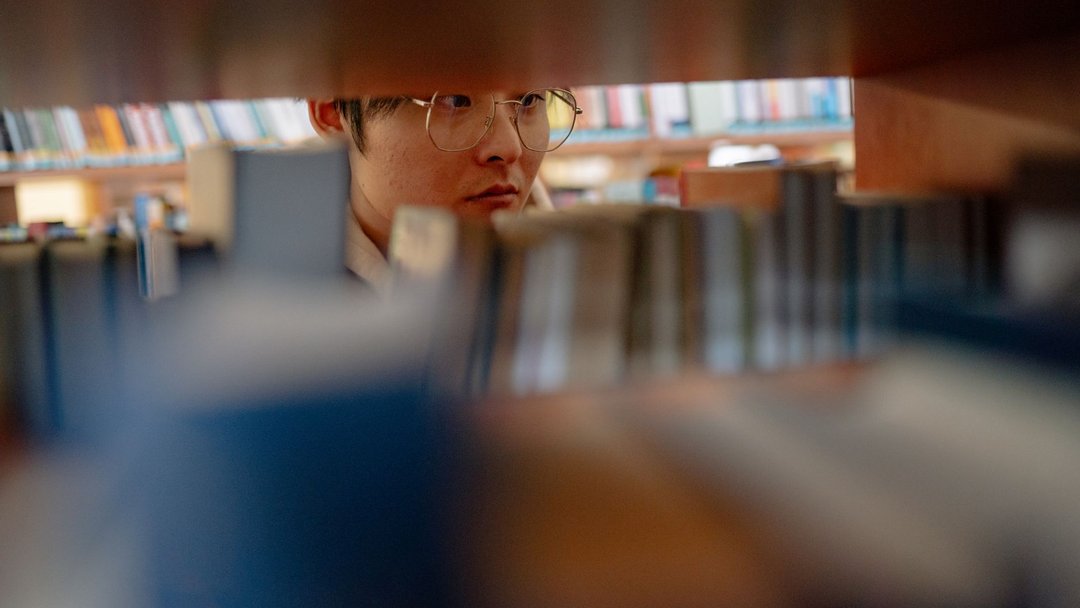 图 / Pexels · Yan Krukau Young man wearing glasses studying intently between library shelves filled with books.