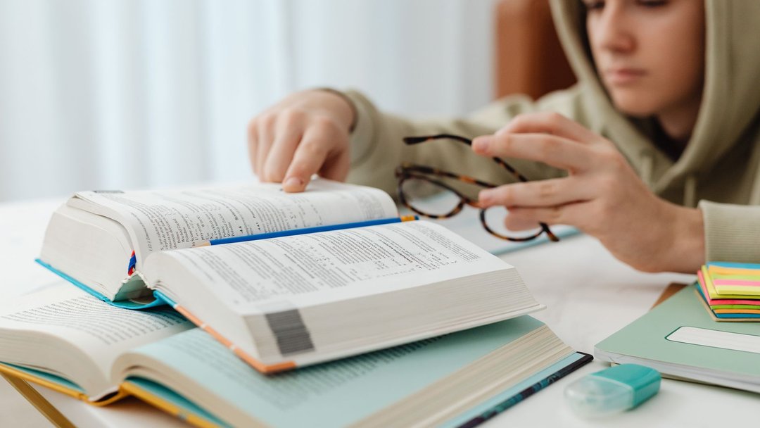 图 / Pexels · https://kaboompics.com/ Focused teenager studying with open textbooks, eyeglasses, and notes.