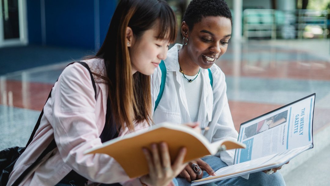 图 / Pexels · Zen Chung Young content multiethnic best female friends speaking while watching textbook on street stairs in city