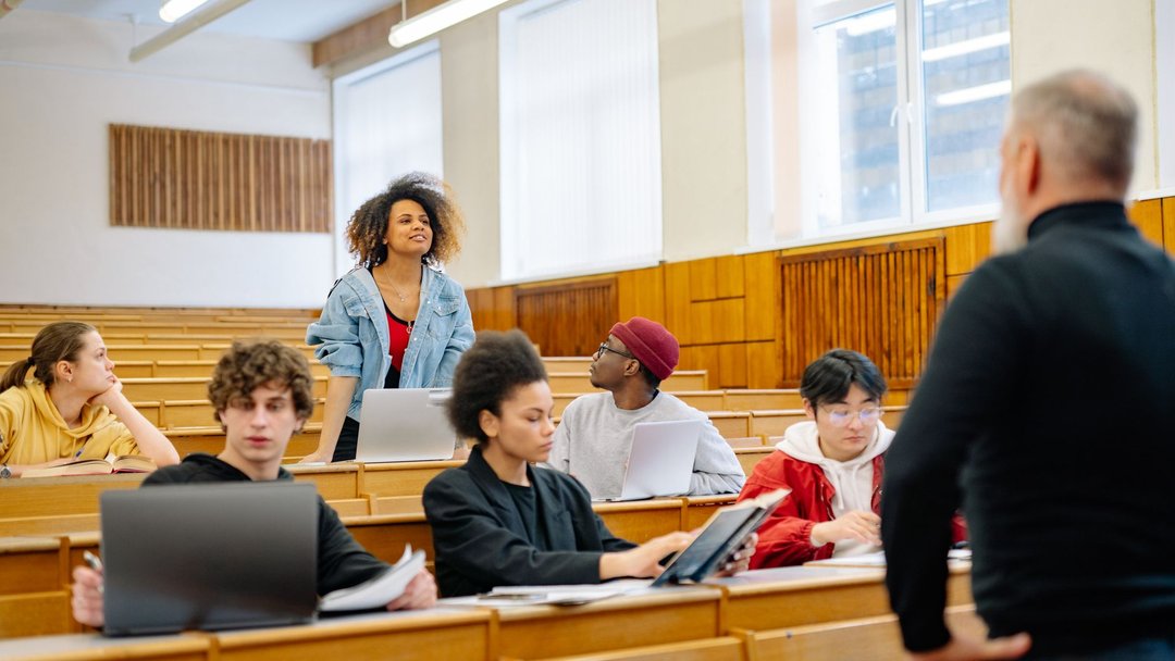A diverse group of university students actively participating in a lecture, engaging with the professor.