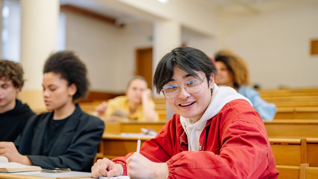 图 / Pexels · Yan Krukau Cheerful student wearing glasses seated in a university lecture hall takes notes during a class.