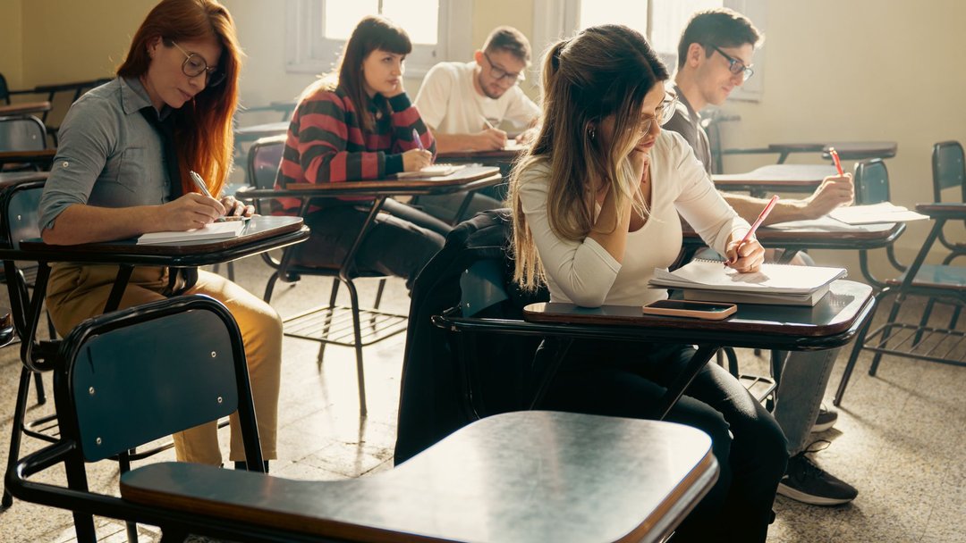 图 / Pexels · Eduard Perez A diverse group of university students focuses on their studies in a sunlit classroom setting.
